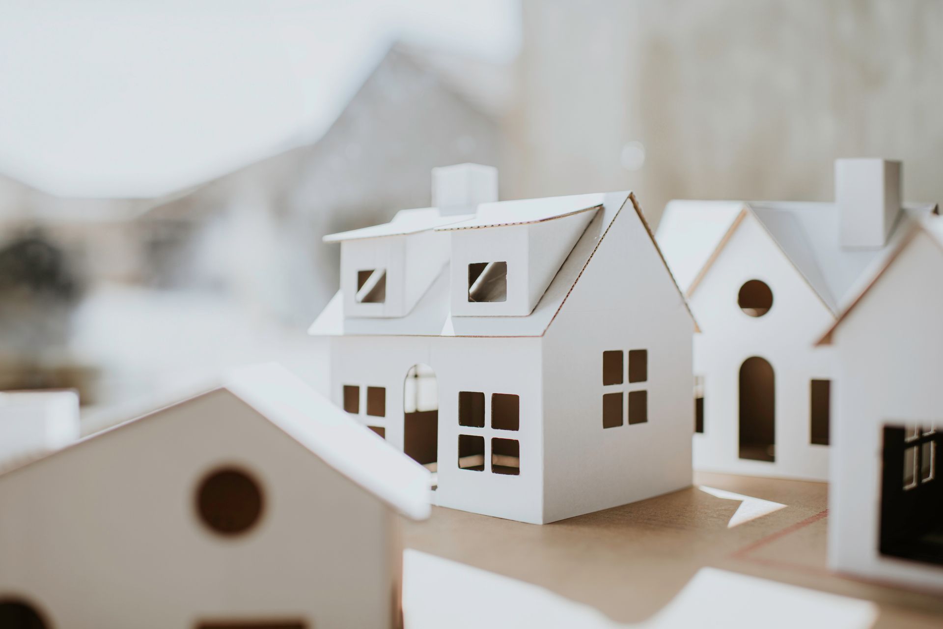 White paper model houses arranged on a brown surface, with blurry background.
