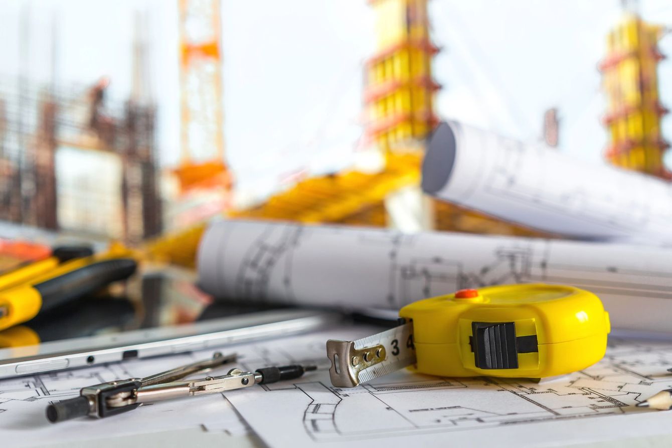 Progetti di costruzione con un metro a nastro giallo, una matita e planimetrie arrotolate su un tavolo da disegno.