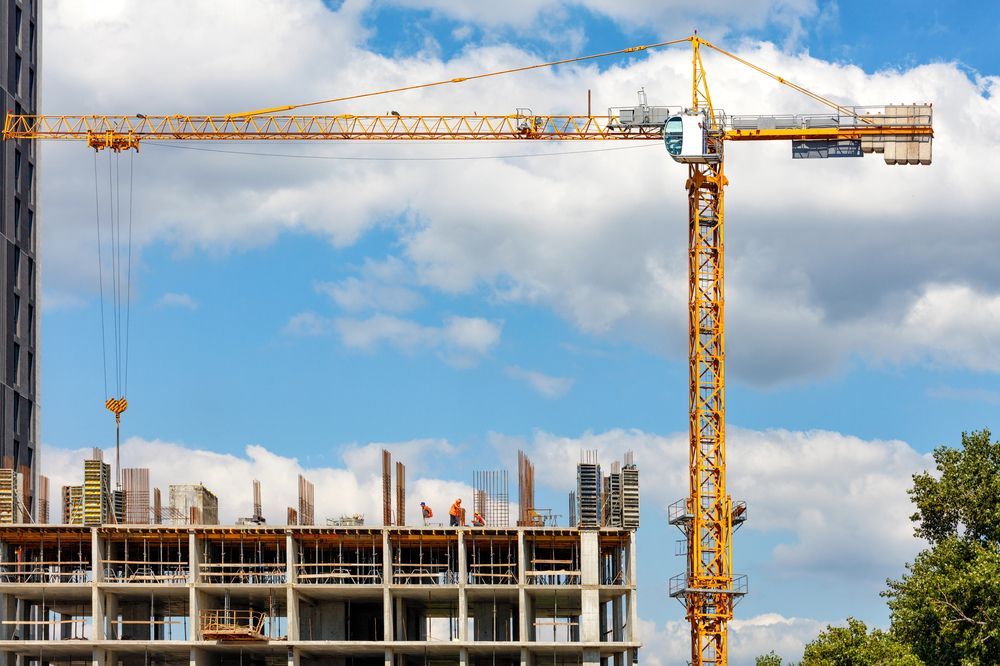 Cantiere edile con una gru a torre gialla sopra un edificio in cemento parzialmente costruito, sotto un cielo azzurro.