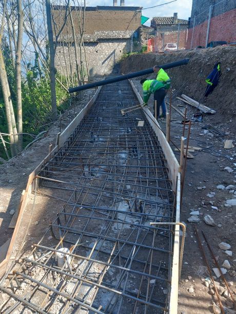 Gli operai edili versano il calcestruzzo in una cassaforma per barre d'armatura per una scala inclinata all'aperto.