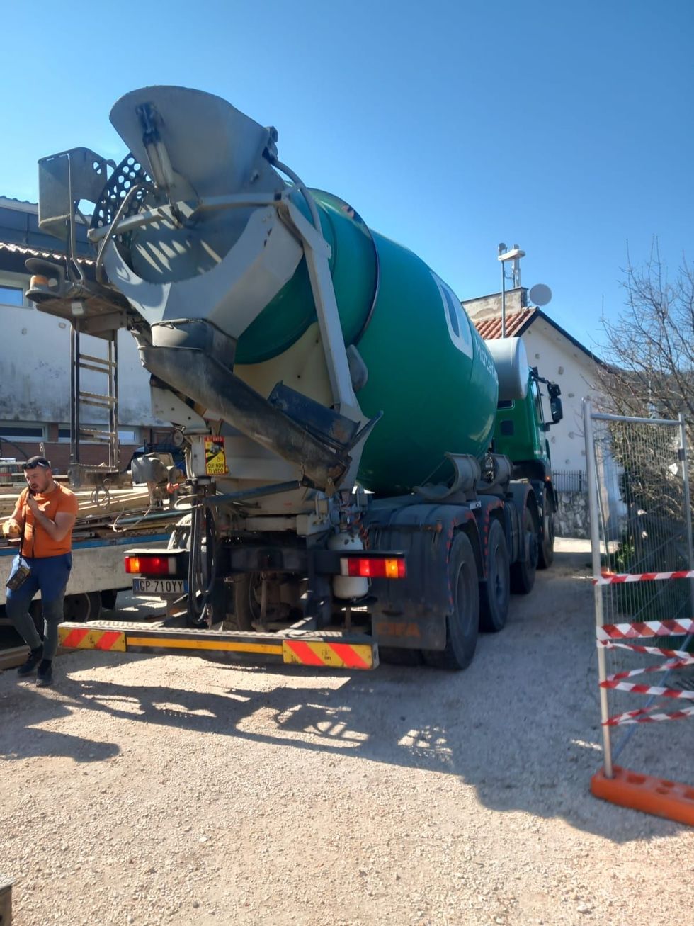 Un camion betoniera ha fatto retromarcia in un cantiere, con operai e barriere arancioni nelle vicinanze.