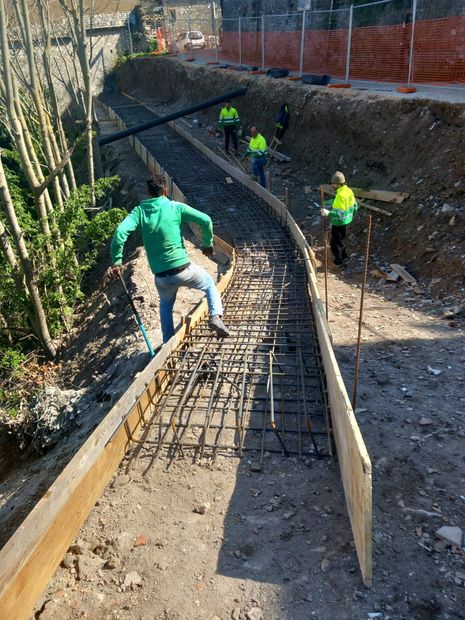Operai versano calcestruzzo in una cassaforma curva in un cantiere edile.