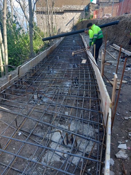 Un operaio con una giacca fluorescente costruisce all'aperto una scala in cemento con barre d'armatura e casseforme in legno.