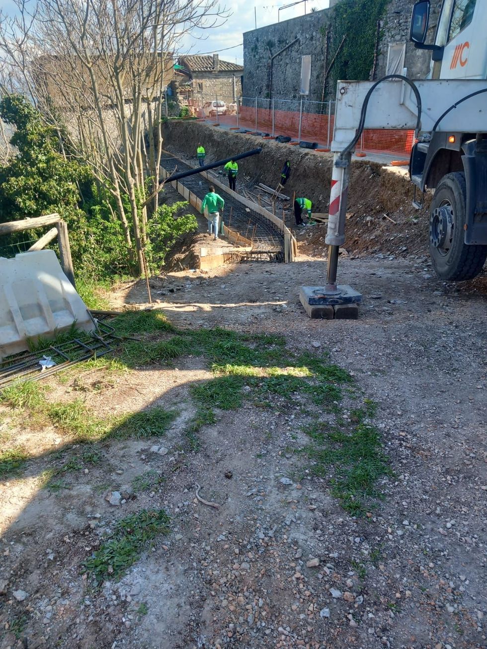 Sentiero sterrato accanto a una casa con piccoli segnali verdi e un grosso veicolo parcheggiato sulla destra.