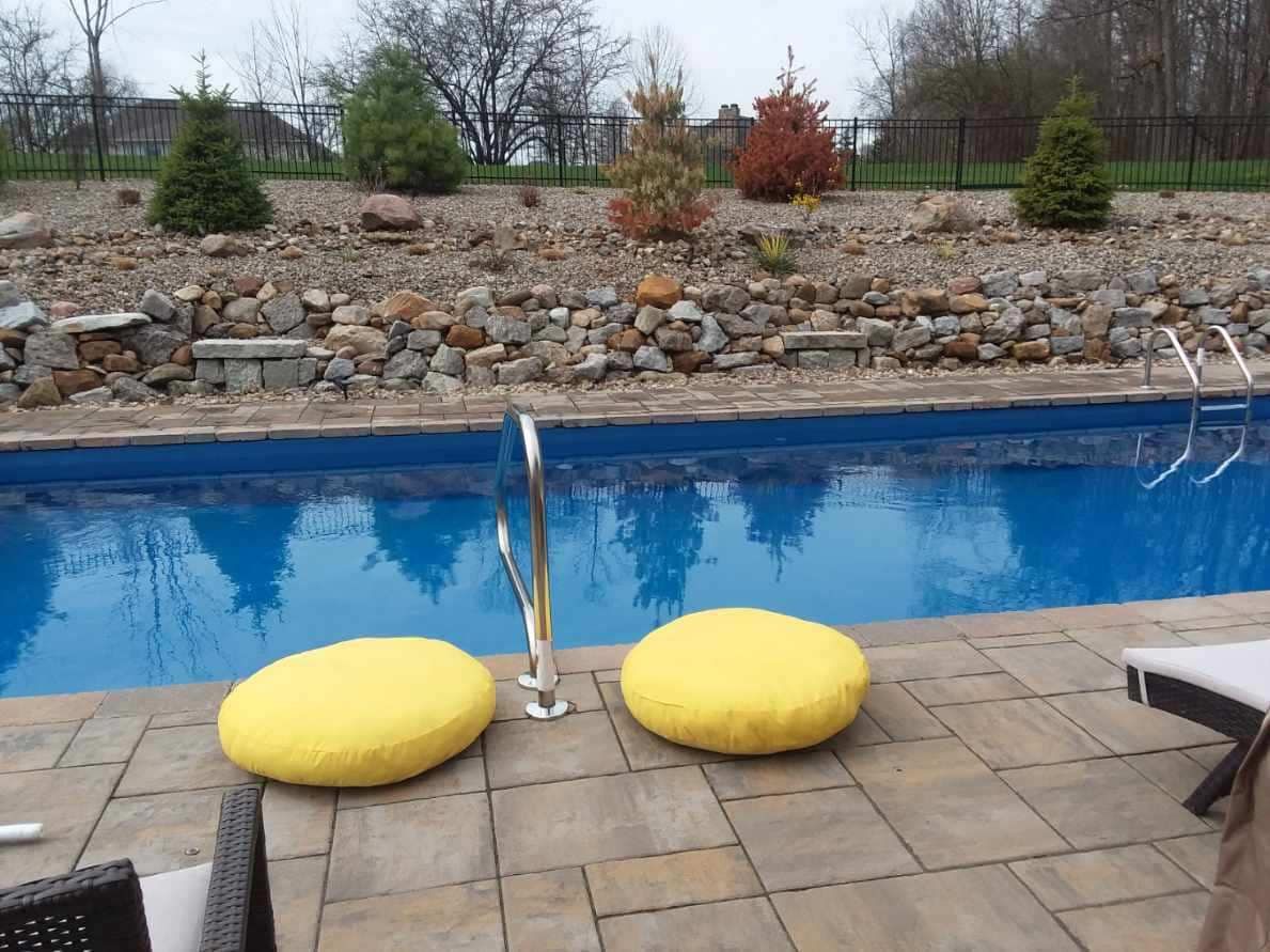 Two yellow cushions on patio by a blue pool and rock garden.