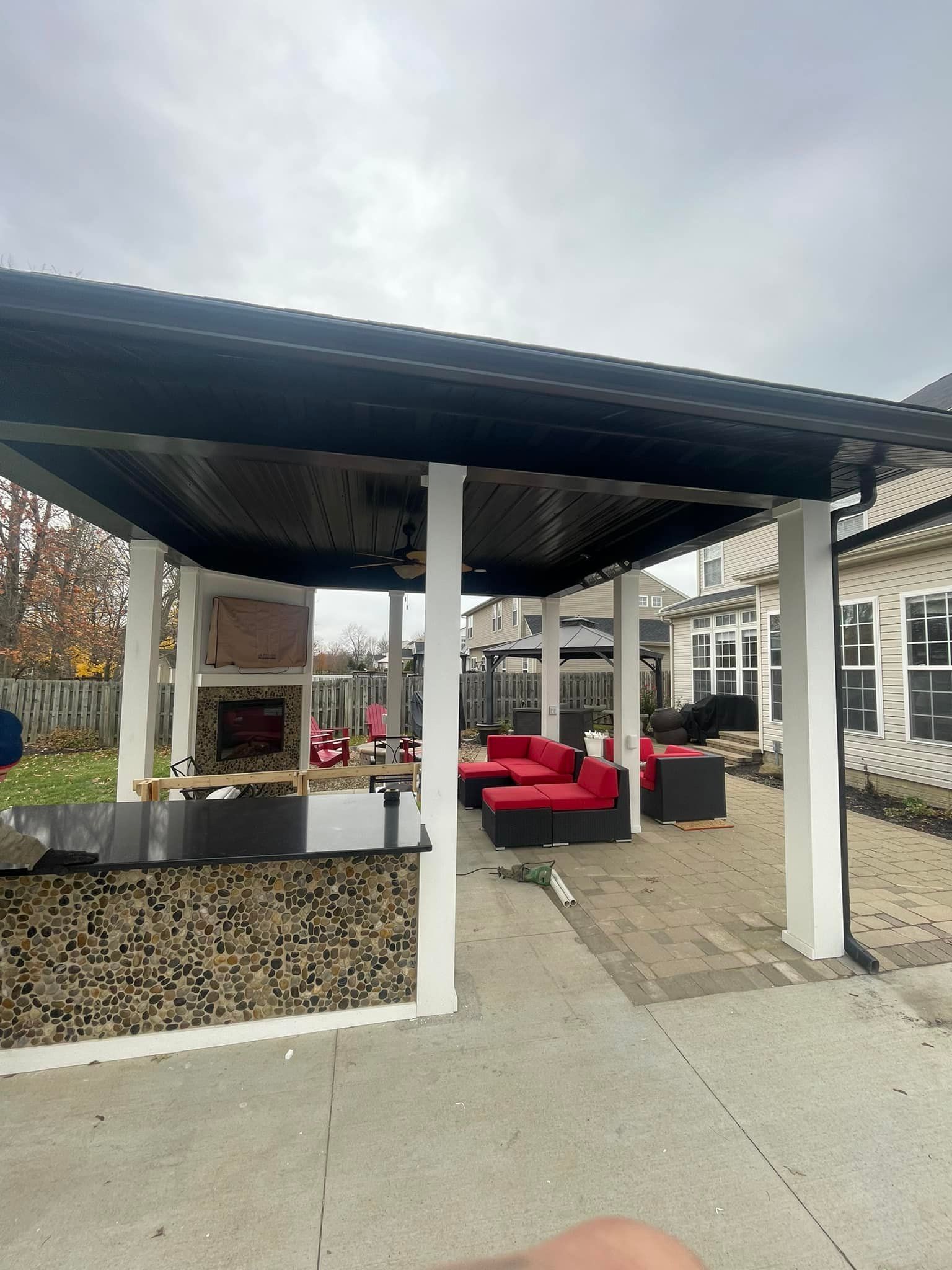 Outdoor patio with red seating, fireplace, and bar under a black-roofed structure with white columns.