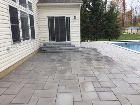 A grey patio with a pool and a house with a sliding glass door and steps.