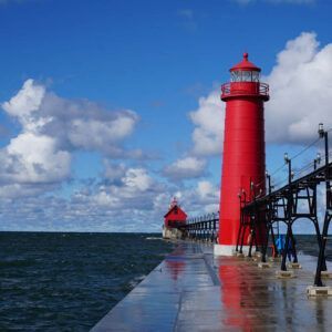 A red lighthouse is sitting on top of a pier next to the ocean.