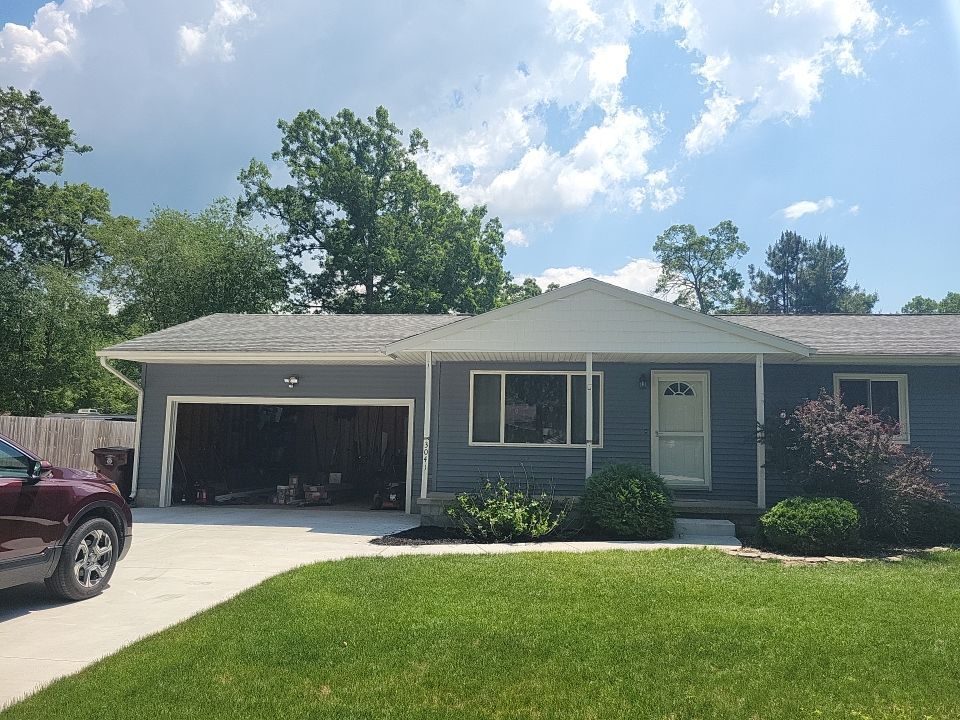 A car is parked in front of a blue house with a garage.