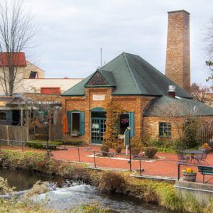 A brick building with a green roof and a chimney next to a river.