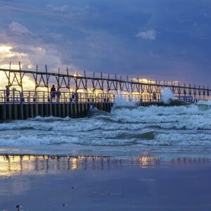 A pier overlooking the ocean at sunset with people standing on it.