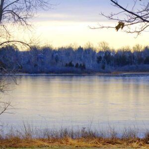 A frozen lake with trees in the background and a sunset in the background.