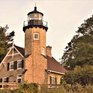 A lighthouse is sitting on top of a brick building surrounded by trees.