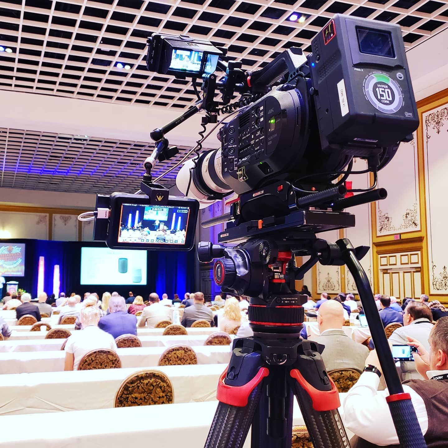A camera is sitting on a tripod in front of a crowd of people.