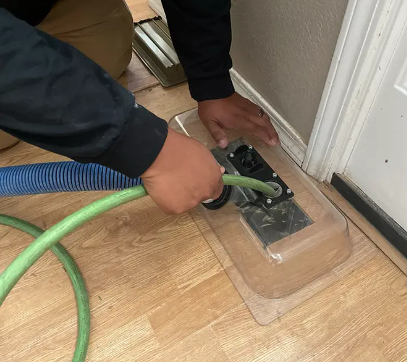 A man is standing on a ladder cleaning an air vent.