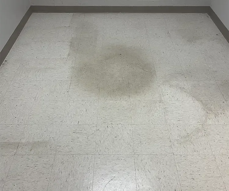 A white tile floor with a stain on it in a room.