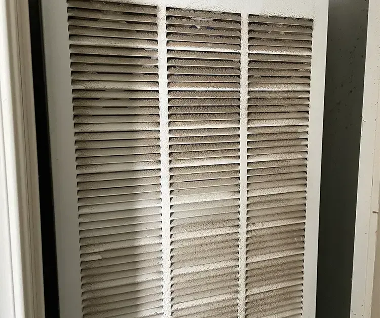 A close up of a dirty air filter on a wall.