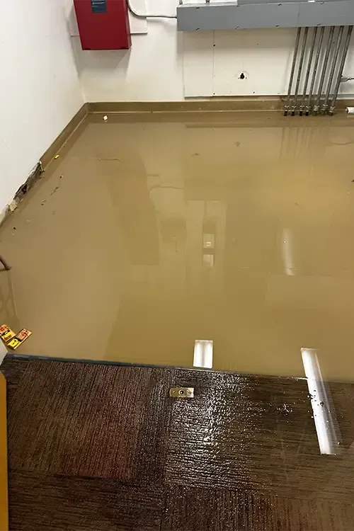 A flooded room with a brown floor and a red fire extinguisher on the wall.
