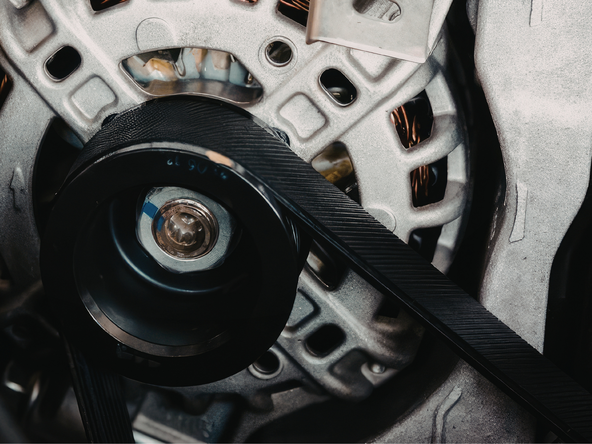 Close-up of a rubber serpentine belt threaded through engine pulleys to power the alternator 