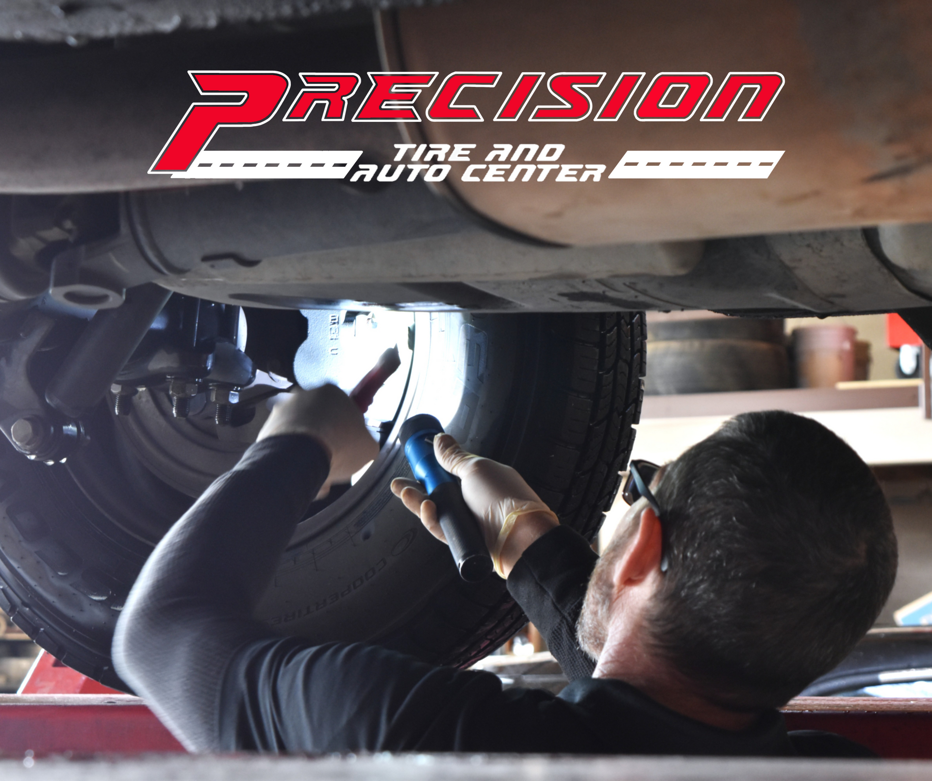 Precision Tire employee using a flashlight to inspect car brakes under the vehicle, ensuring safety