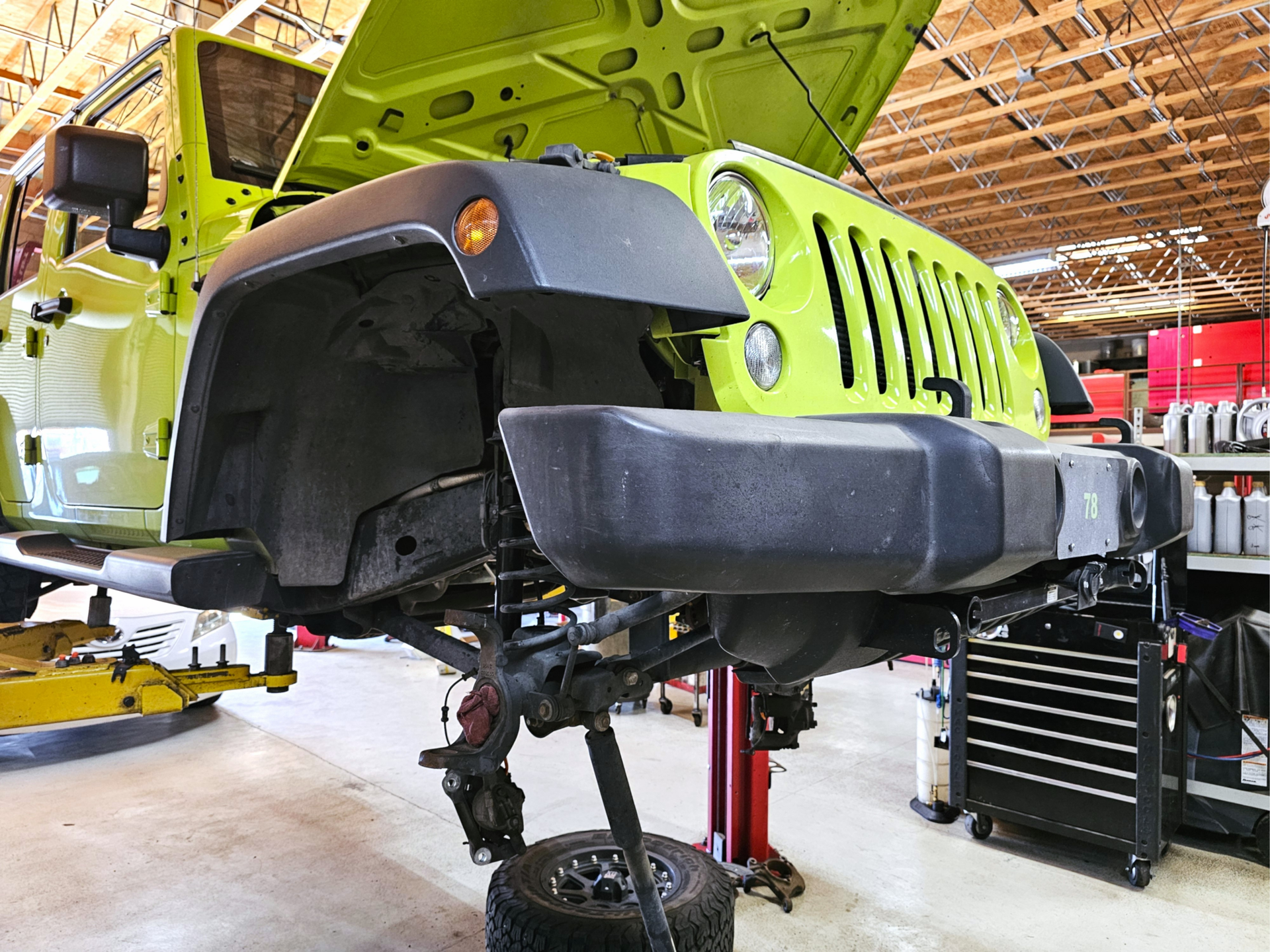Jeep on lift with front end exposed showing suspension, steering, & wheel components for maintenance