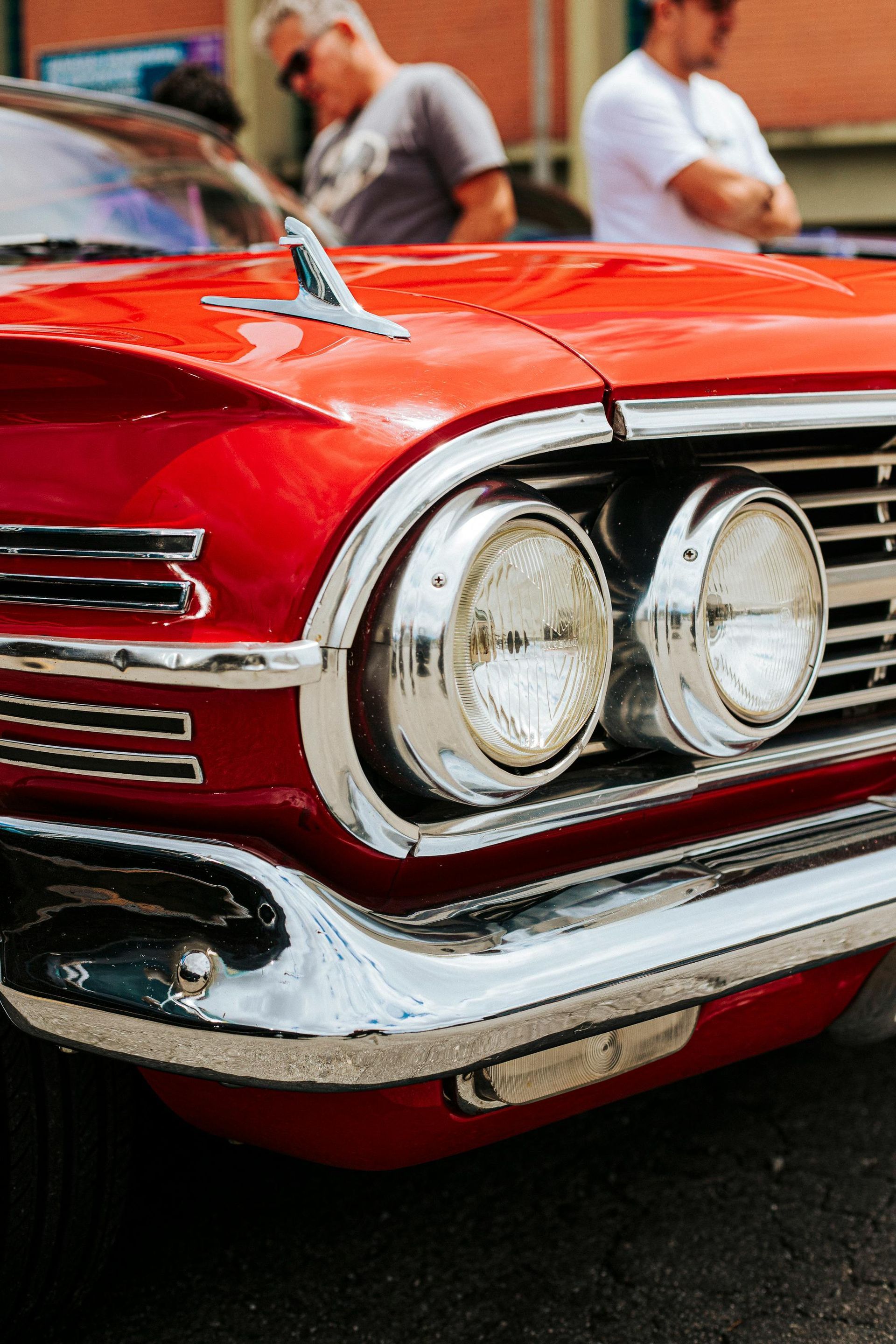 Close-up of a shiny red classic car front with chrome grille and round headlights outdoors