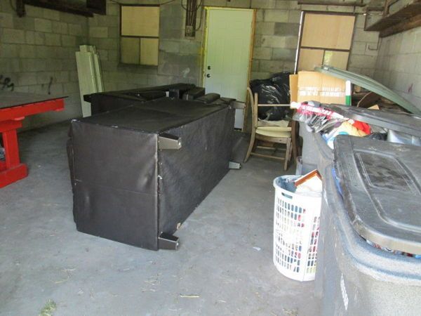 A couch is sitting in a garage next to a trash can