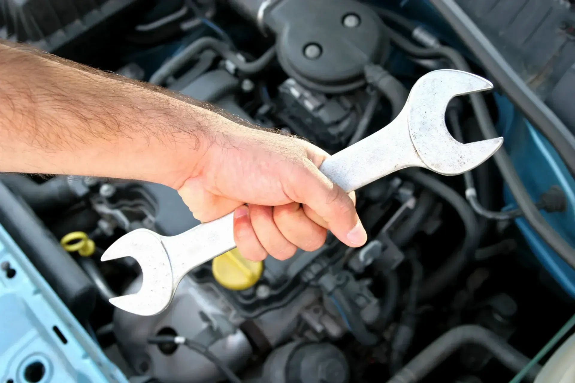 A person is holding two wrenches in front of a car engine