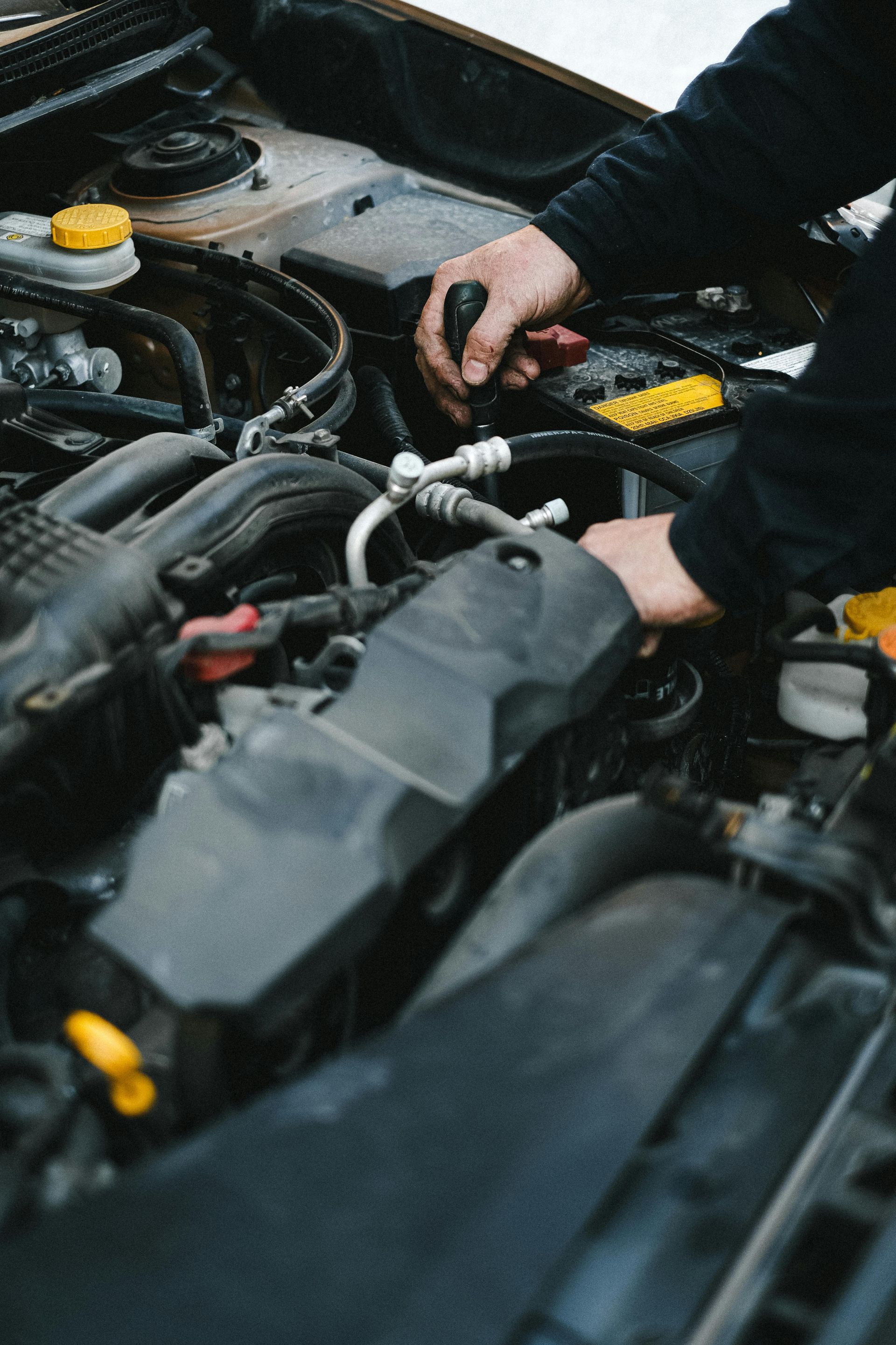 A man is working on the engine of a car with a screwdriver.