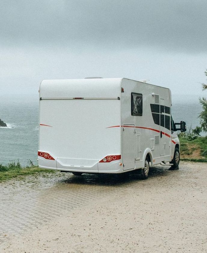 A white rv is parked on a gravel road near the ocean.