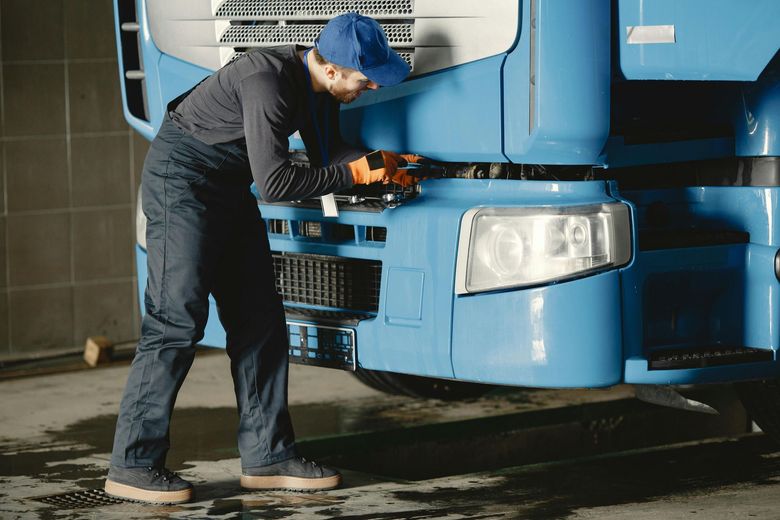 A man is working on the front of a blue truck.