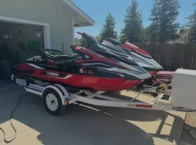 A red jet ski is parked on a trailer in front of a garage.