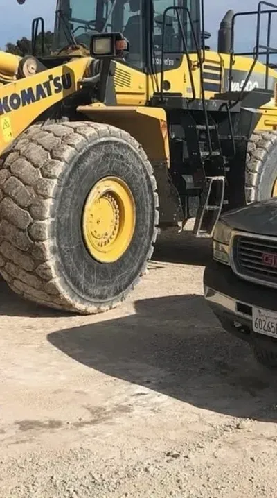 A komatsu wheel loader is parked next to a gmc truck.