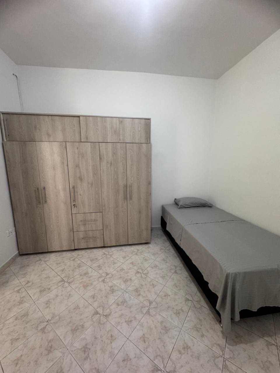 Dormitorio con gran armario de madera y cama individual con ropa de cama gris.