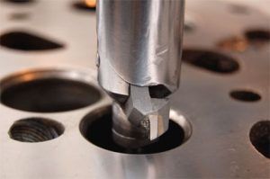 Primer plano de una máquina herramienta escariando un asiento de válvula en una culata, metal plateado sobre metal.