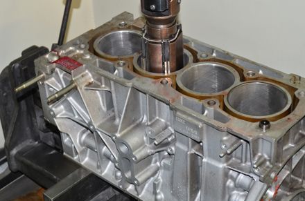 Bloque del motor siendo pulido por una máquina, mostrando los orificios de los cilindros y la estructura circundante.