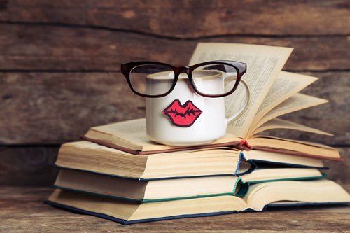 occhiali da vista con montatura tonda sopra una pila di libri e vicino a una tazza da caffe