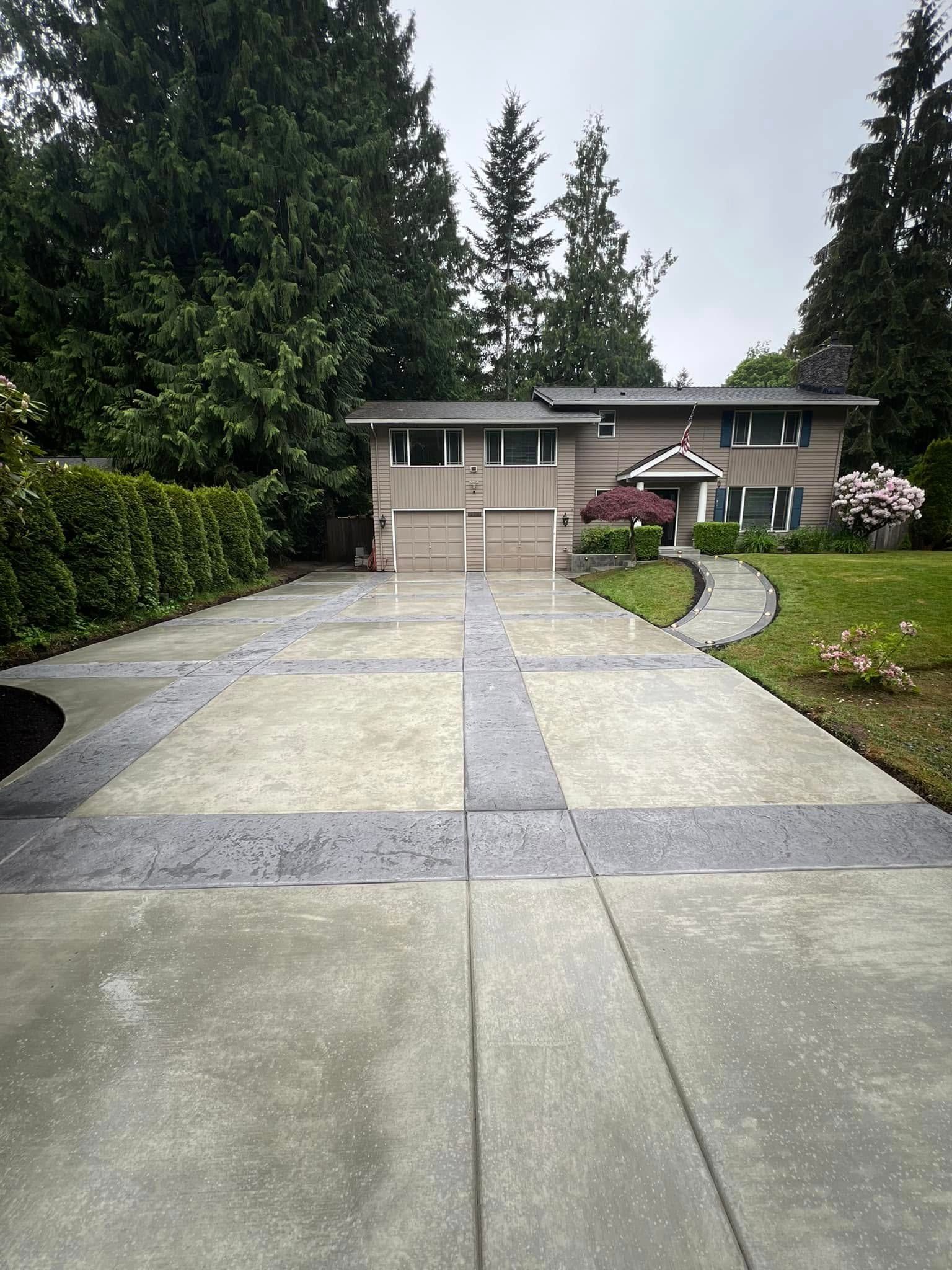 A concrete driveway leading to a large house surrounded by trees.