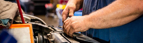 Mechanic working on a car engine, hands visible. Air filter, red tools, and blue shirt present | Rick's Automotive