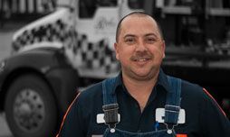 Smiling tow truck driver in blue overalls, truck in background. | Rick's Automotive