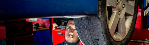 Mechanic looking at car's tire, working under the vehicle, surrounded by equipment. | Rick's Automotive