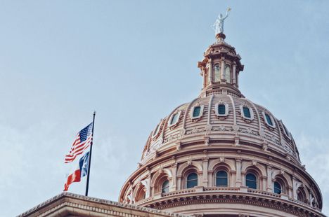 Texas State Capitol building dome with American and Texas flags, against a blue sky.