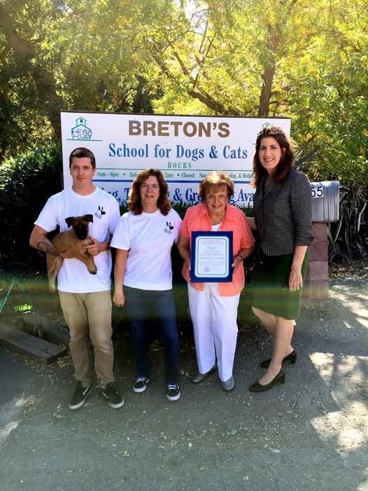People pose in front of a sign for Breton's School for Dogs & Cats. One person holds a small dog