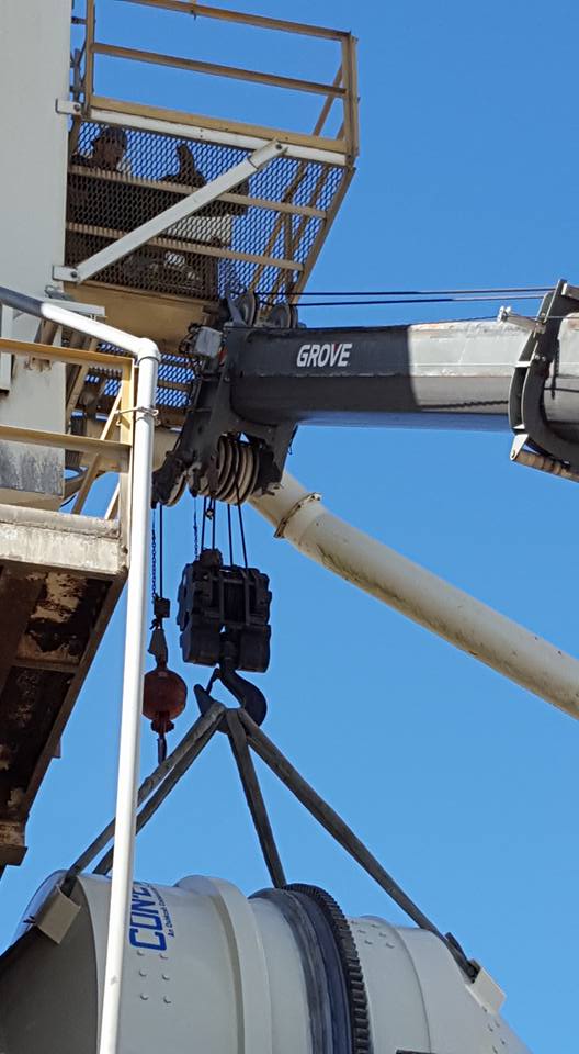 A crane lifts a black bucket under a metal platform against a clear blue sky.