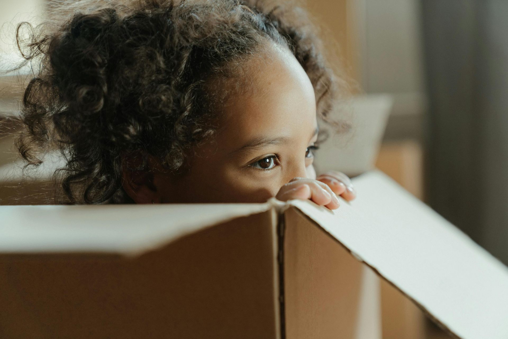 Child peeking over a moving box — diplomatic family moving London with The Mover Group