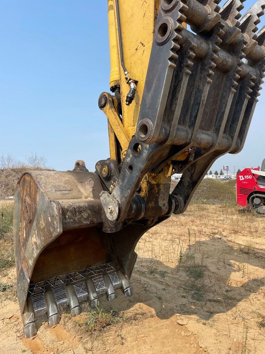 Yellow excavator bucket and claw, digging into dirt, blue sky background.
