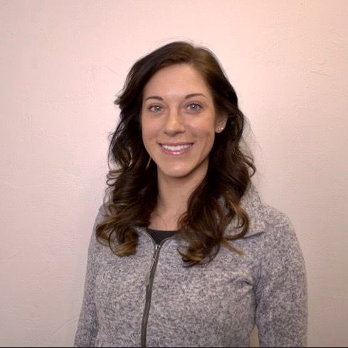 A woman in a grey jacket is smiling for the camera.