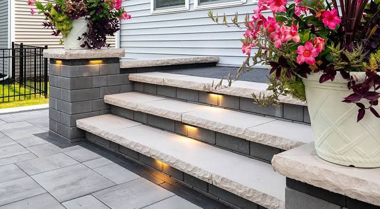 Lit stone walkway with garden beds and lawn, illuminated by embedded and post lights.