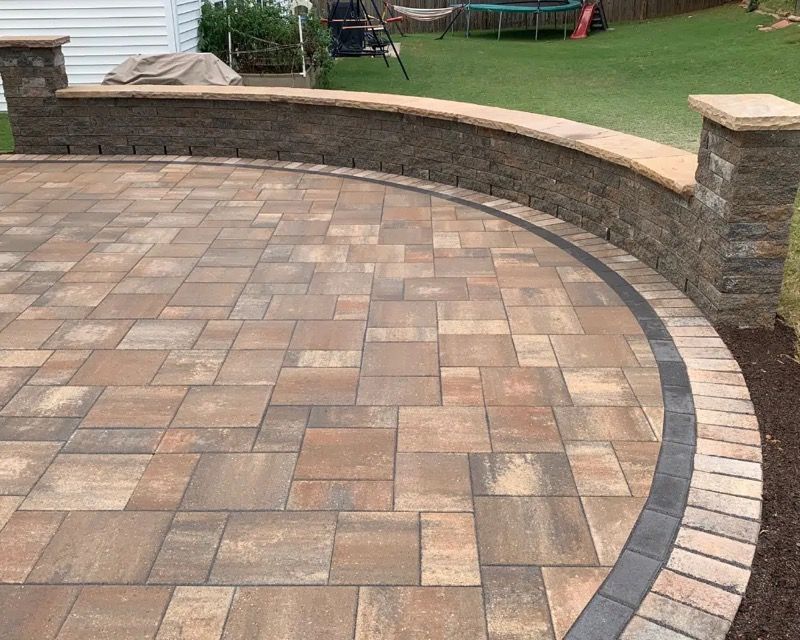 Two-tiered gray block retaining wall with green bushes on top, planted in dark soil.