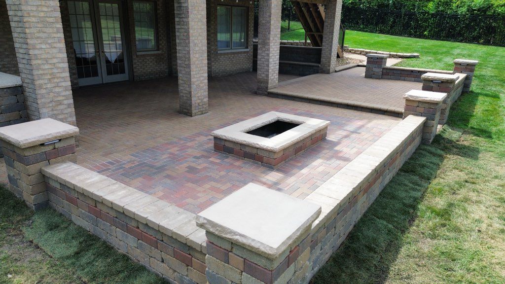 Stone fire pit and gazebo in a landscaped backyard at dusk, with trees in the background.